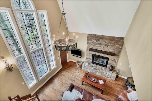 living room with a fireplace, a towering ceiling, an inviting chandelier, wood finished floors, and baseboards