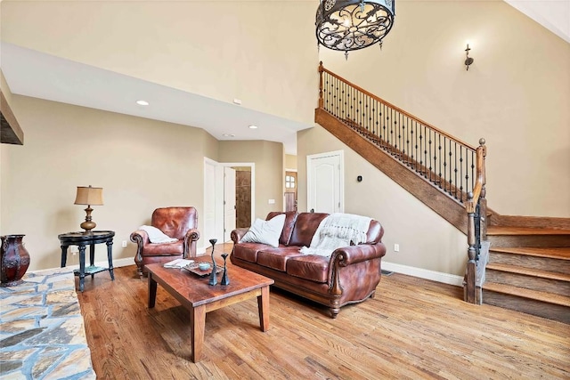 living room featuring a high ceiling, baseboards, light wood finished floors, and stairs