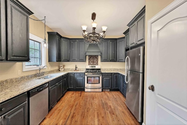 kitchen featuring light wood-style flooring, stainless steel appliances, a sink, decorative light fixtures, and an inviting chandelier