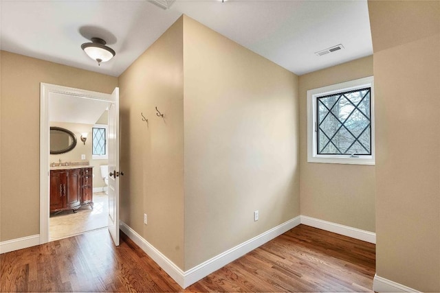 hall featuring a sink, wood finished floors, visible vents, and baseboards