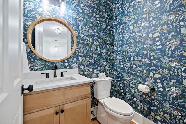 half bathroom featuring toilet, wallpapered walls, and vanity