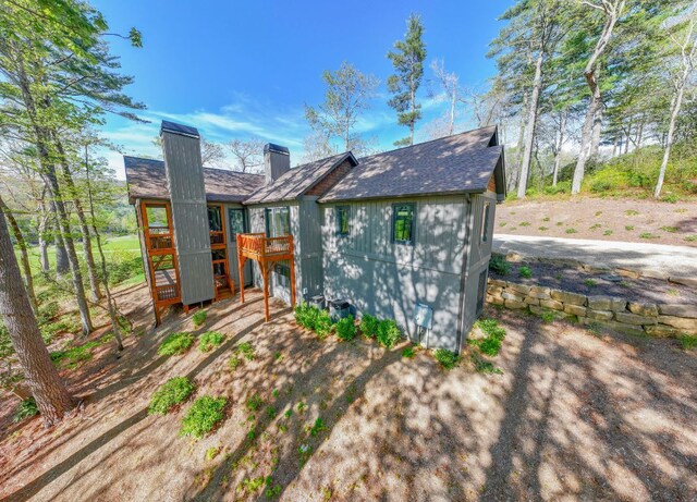 back of property with a wooden deck, a shingled roof, and a chimney