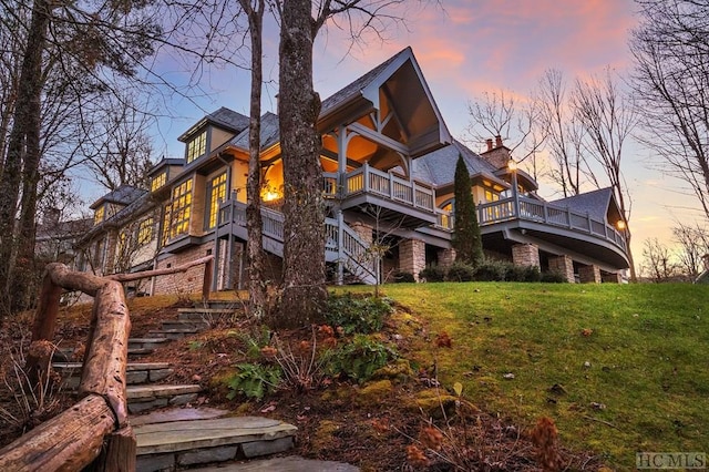 back house at dusk featuring a lawn and a balcony