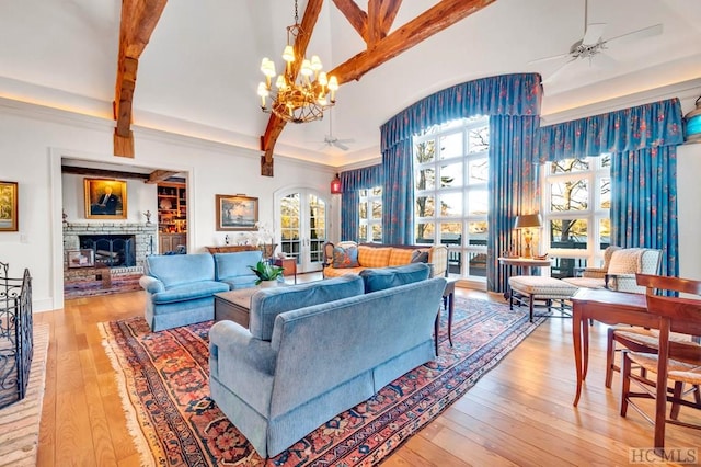 living room with a brick fireplace, ceiling fan with notable chandelier, and beamed ceiling