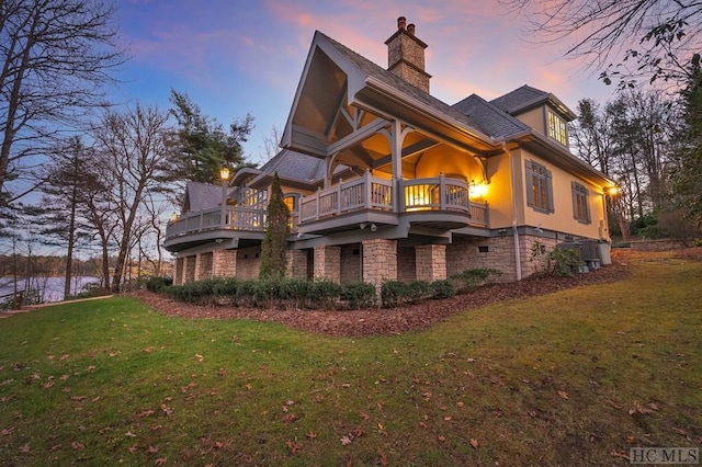 back house at dusk featuring a balcony and a lawn