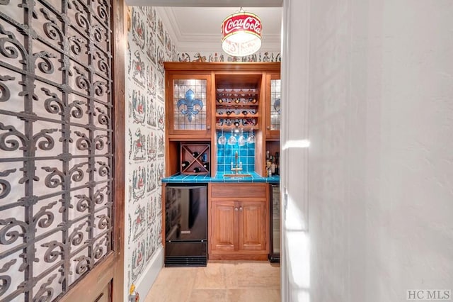 bar with crown molding, fridge, tile counters, and sink