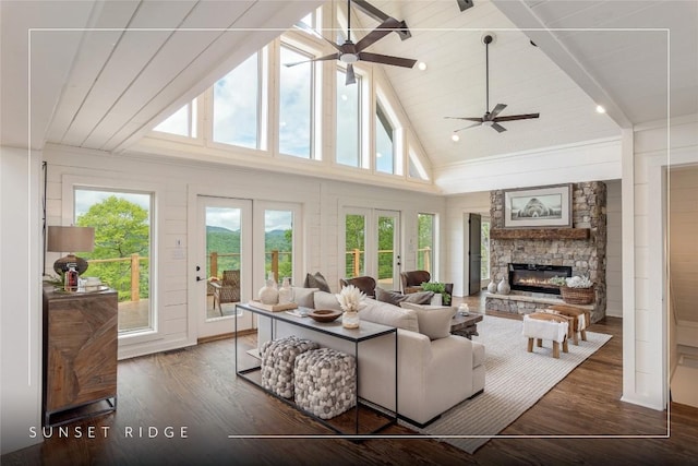 living area with high vaulted ceiling, french doors, wood finished floors, a stone fireplace, and ceiling fan