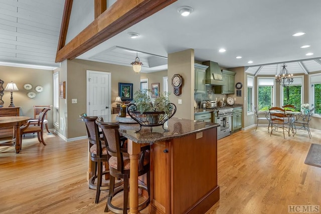 kitchen featuring stainless steel stove, dark stone countertops, hanging light fixtures, green cabinetry, and custom exhaust hood