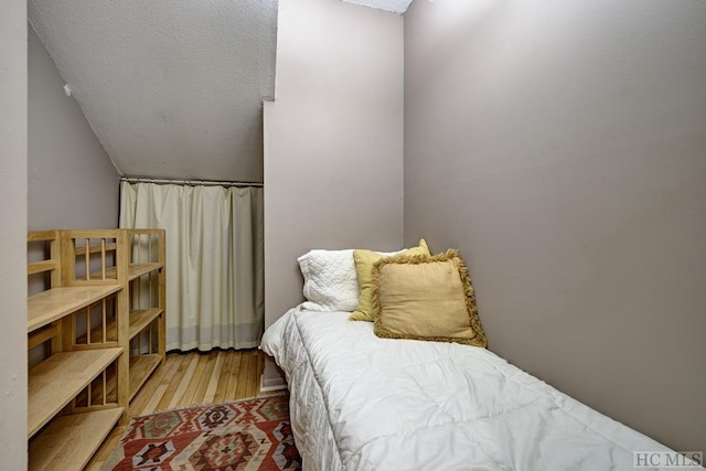 bedroom featuring light hardwood / wood-style floors, vaulted ceiling, and a textured ceiling