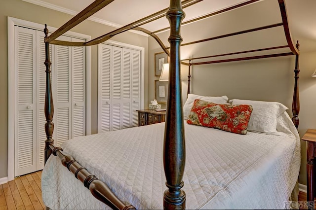 bedroom featuring light hardwood / wood-style floors, crown molding, and two closets