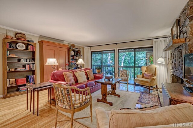 living room featuring crown molding, a stone fireplace, and light hardwood / wood-style floors