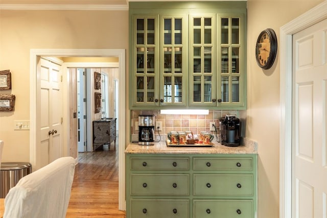 bar featuring crown molding, green cabinets, light hardwood / wood-style floors, and decorative backsplash