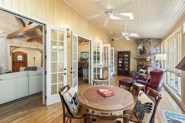 dining room with french doors, wood walls, light hardwood / wood-style flooring, wooden ceiling, and vaulted ceiling with skylight