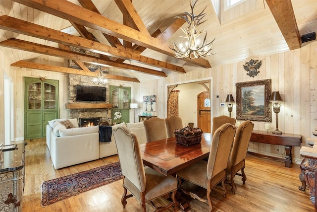 dining space featuring an inviting chandelier, wooden walls, a stone fireplace, and light hardwood / wood-style flooring