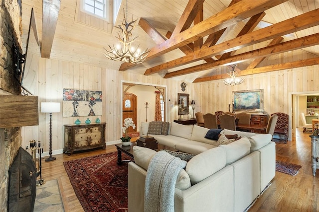 living room with beam ceiling, hardwood / wood-style flooring, an inviting chandelier, and wood walls