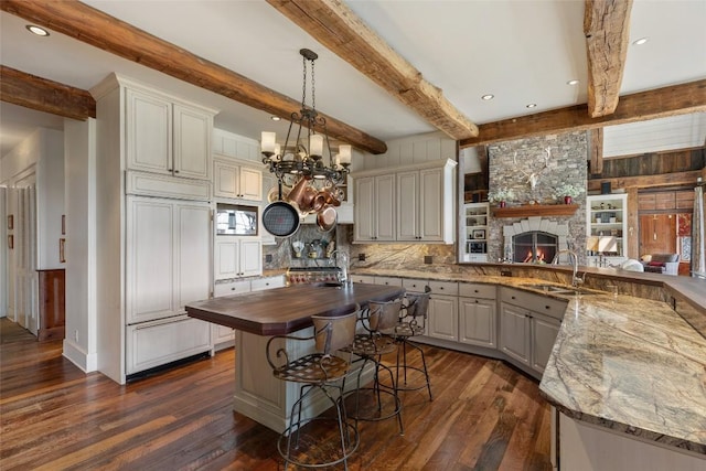 kitchen with built in appliances, beam ceiling, dark wood-type flooring, a sink, and wood counters