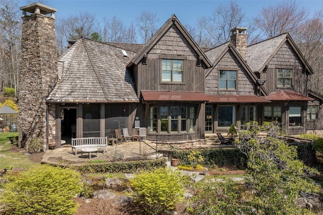 rear view of property with board and batten siding, a patio area, and a chimney