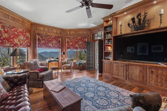 living area with wood walls, ceiling fan, and wood finished floors