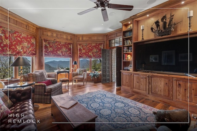 living room with ceiling fan, wood finished floors, and wooden walls