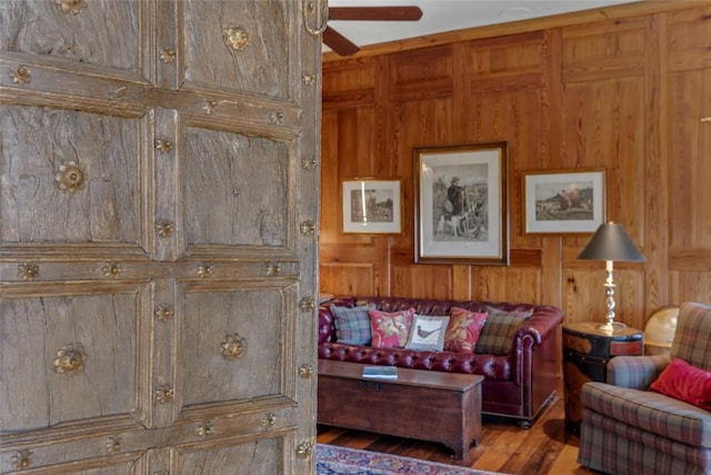 living area featuring ceiling fan, wood walls, and wood finished floors