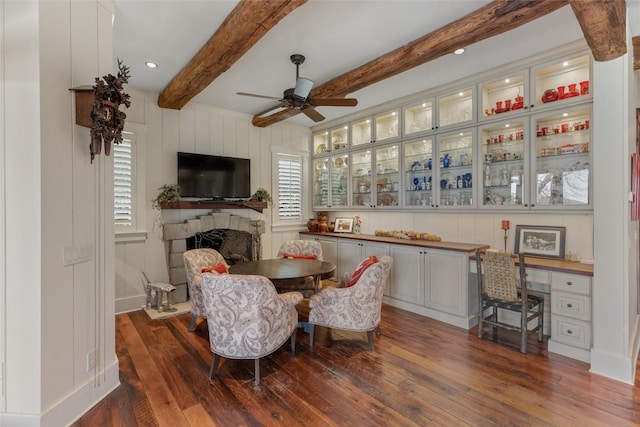 dining area with a decorative wall, a fireplace, beamed ceiling, ceiling fan, and dark wood-style floors