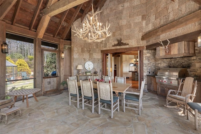 dining area featuring stone floors, high vaulted ceiling, a notable chandelier, and beamed ceiling