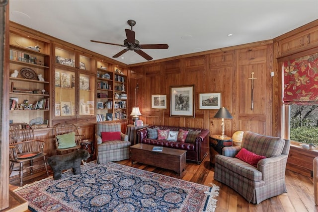 living area with wood-type flooring, ceiling fan, and wood walls