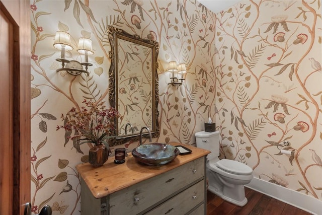 half bath featuring vanity, toilet, baseboards, wallpapered walls, and wood finished floors