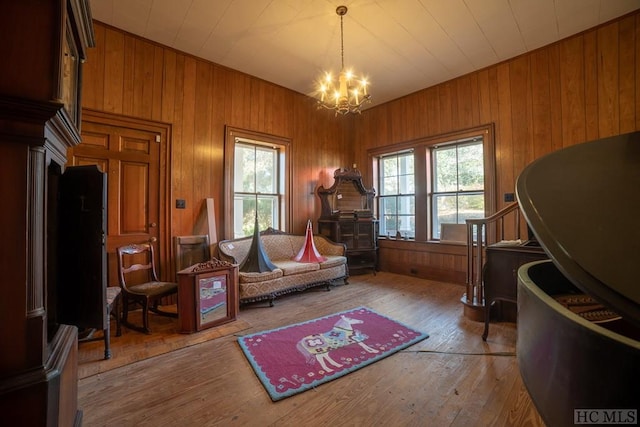 living area with plenty of natural light, a notable chandelier, wooden walls, and light hardwood / wood-style flooring