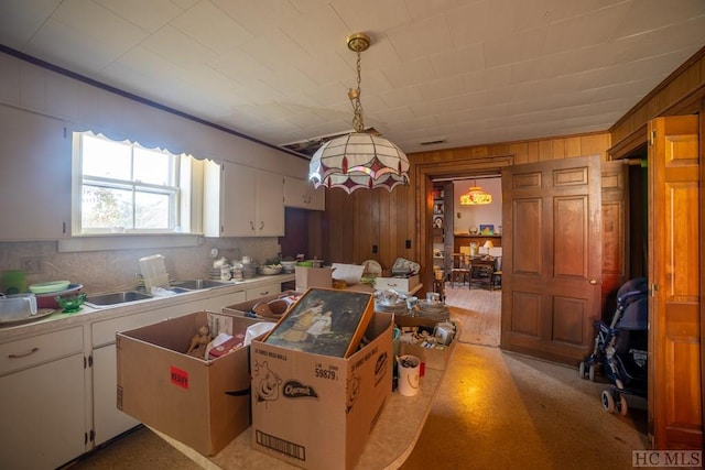 kitchen featuring wooden walls, sink, hanging light fixtures, and white cabinets