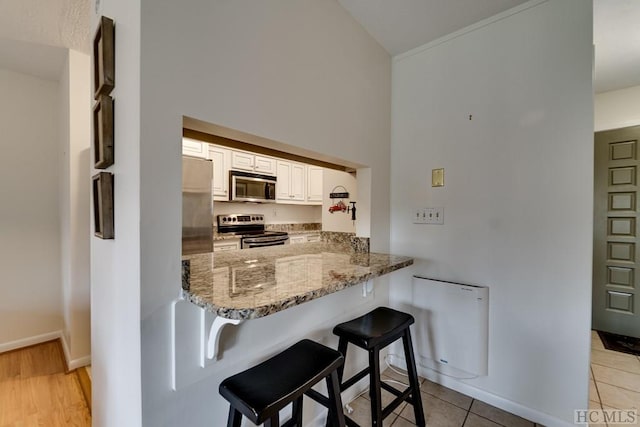 kitchen with a breakfast bar area, stone counters, stainless steel appliances, white cabinets, and kitchen peninsula