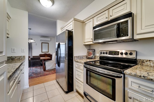 kitchen featuring a wall unit AC, stainless steel appliances, light stone countertops, a textured ceiling, and light tile patterned flooring