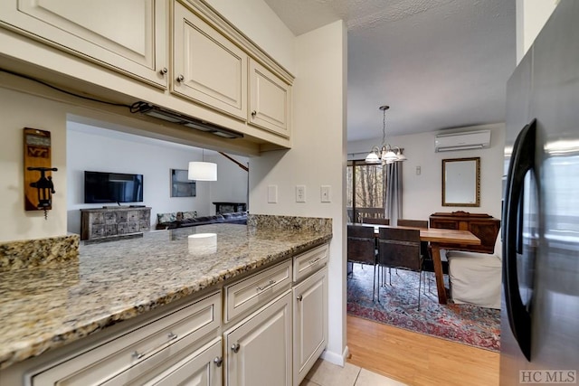 kitchen featuring black refrigerator, a wall mounted AC, cream cabinets, light stone countertops, and a chandelier