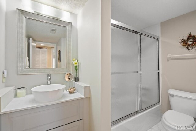 full bathroom featuring combined bath / shower with glass door, vanity, a textured ceiling, tile patterned floors, and toilet