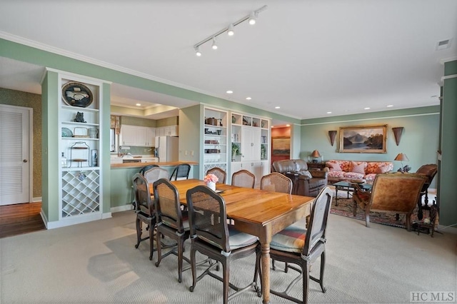 carpeted dining room featuring crown molding and track lighting