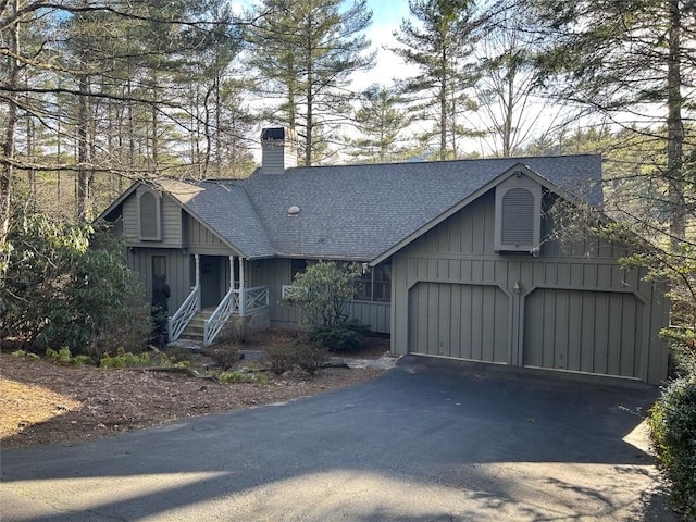 chalet / cabin with driveway, a shingled roof, board and batten siding, and a chimney