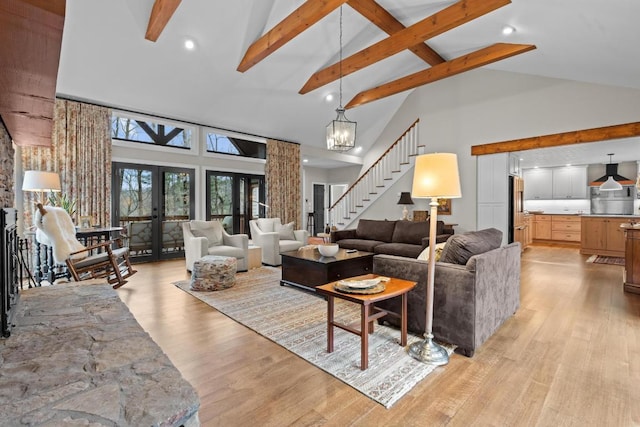 living room with beamed ceiling, stairway, light wood-style flooring, french doors, and an inviting chandelier