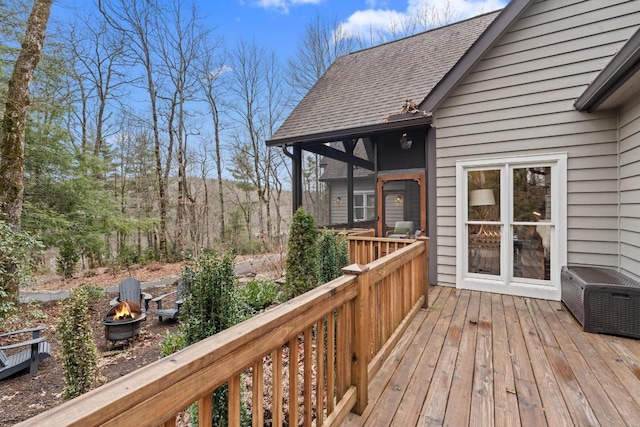 wooden deck featuring an outdoor fire pit and a sunroom