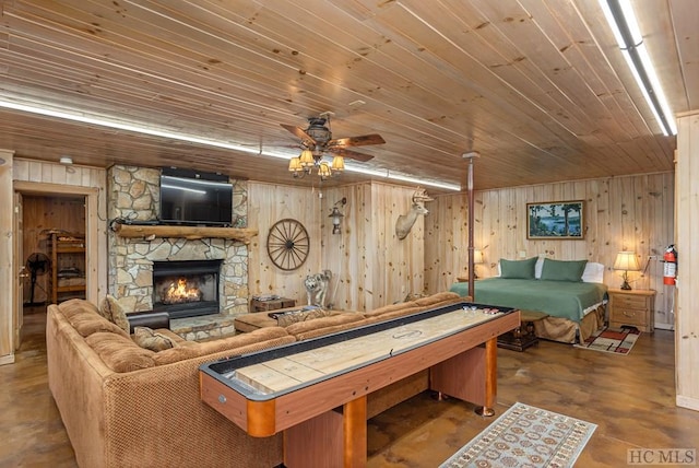 playroom featuring a stone fireplace, concrete flooring, wood walls, wood ceiling, and ceiling fan