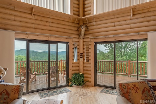 doorway with a mountain view, log walls, a healthy amount of sunlight, and a towering ceiling