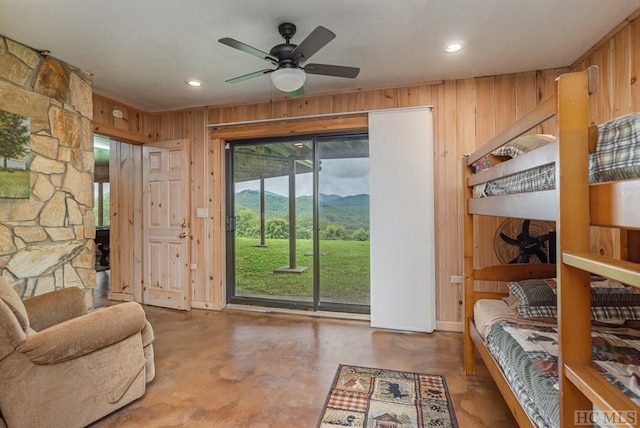 interior space with concrete flooring, a mountain view, wooden walls, and ceiling fan