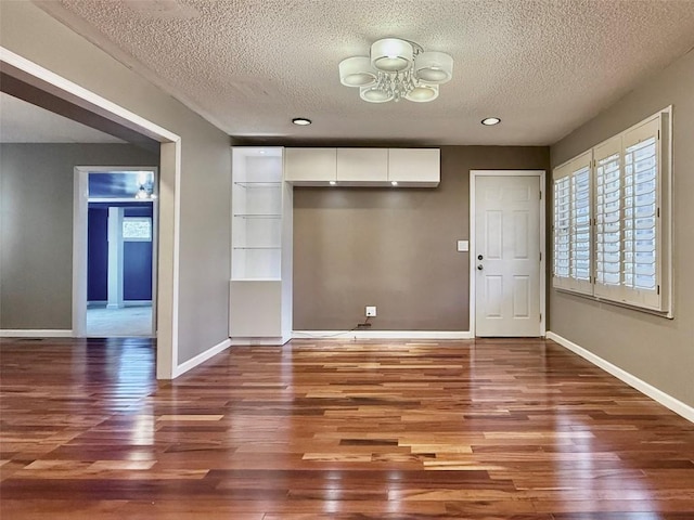 unfurnished dining area with a textured ceiling, wood finished floors, and baseboards