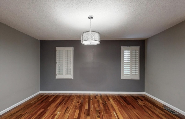 spare room with a textured ceiling, wood finished floors, baseboards, and visible vents