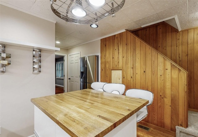 dining space with ornamental molding, visible vents, wood finished floors, wooden walls, and baseboards