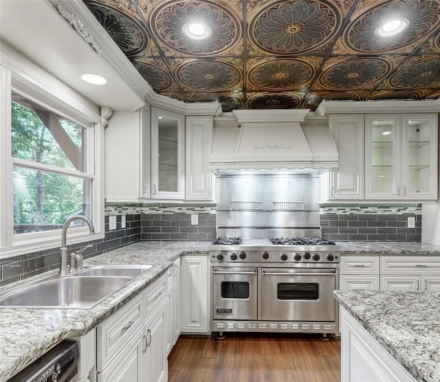kitchen with white cabinetry, double oven range, custom exhaust hood, dishwasher, and a sink