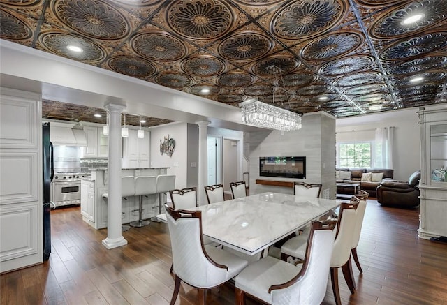 dining room featuring decorative columns, dark wood-type flooring, an ornate ceiling, and a large fireplace