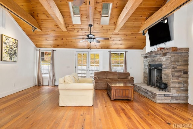 unfurnished living room with wood ceiling, light hardwood / wood-style flooring, lofted ceiling with beams, a stone fireplace, and french doors