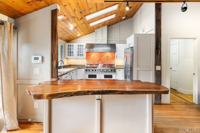 kitchen featuring appliances with stainless steel finishes, butcher block counters, sink, white cabinets, and wall chimney range hood