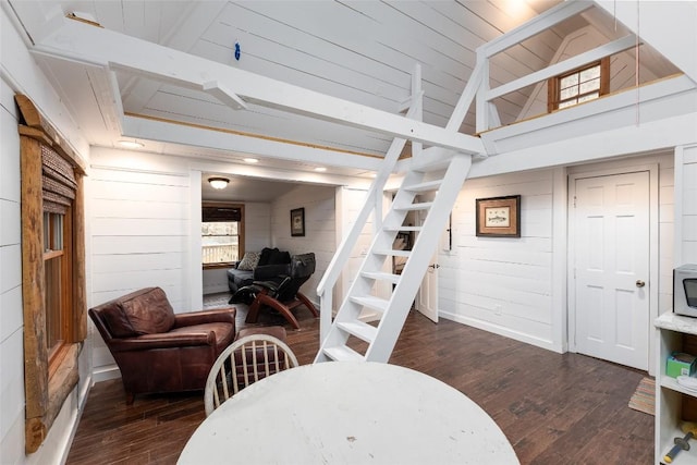 interior space featuring dark wood finished floors, wooden walls, baseboards, and stairs