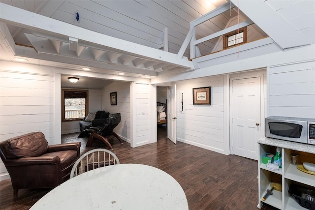 interior space featuring wooden walls, dark wood-style flooring, lofted ceiling with beams, and baseboards